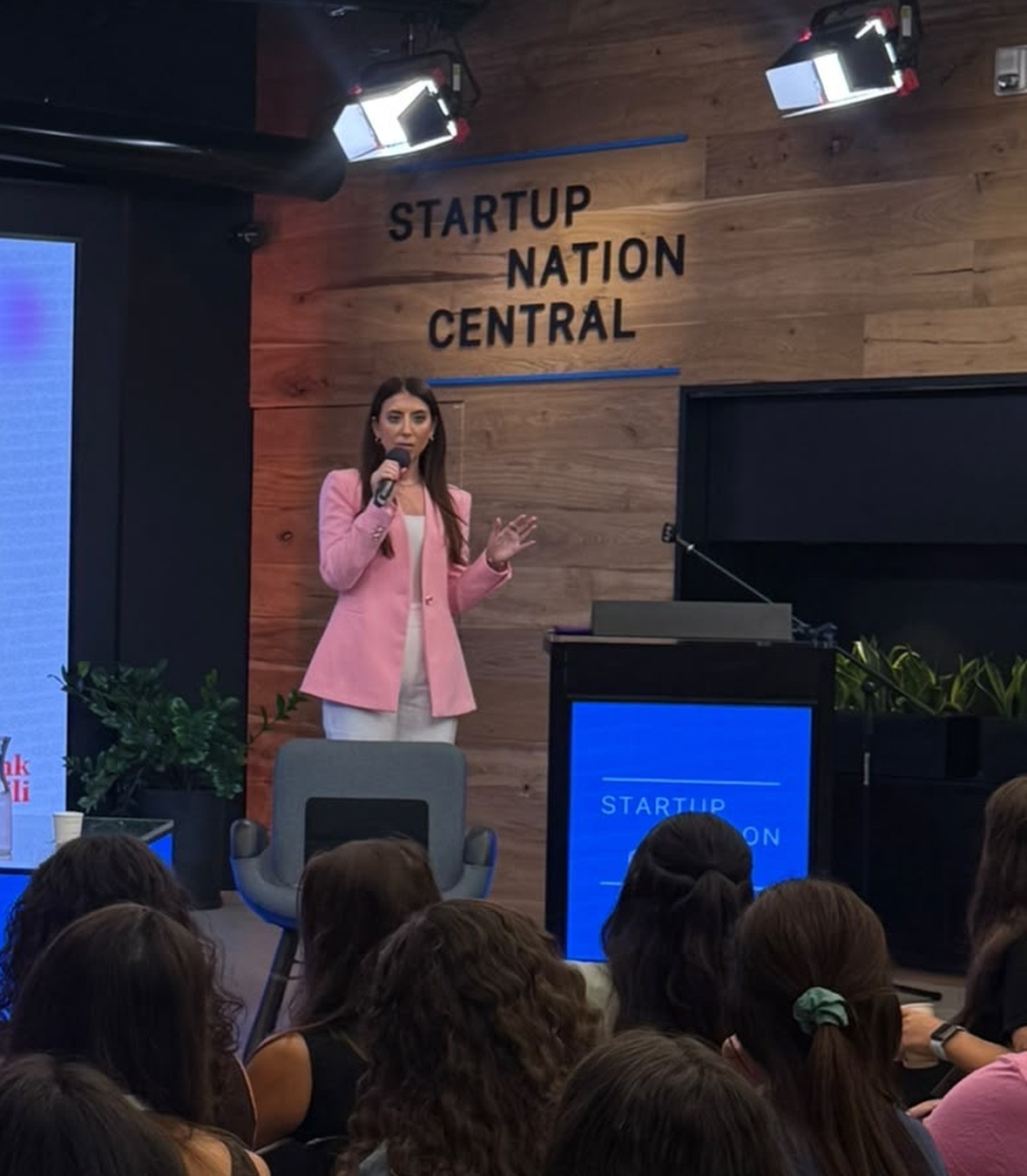 Alison Hoffer speaking with a microphone to an audience at Startup Nation Central